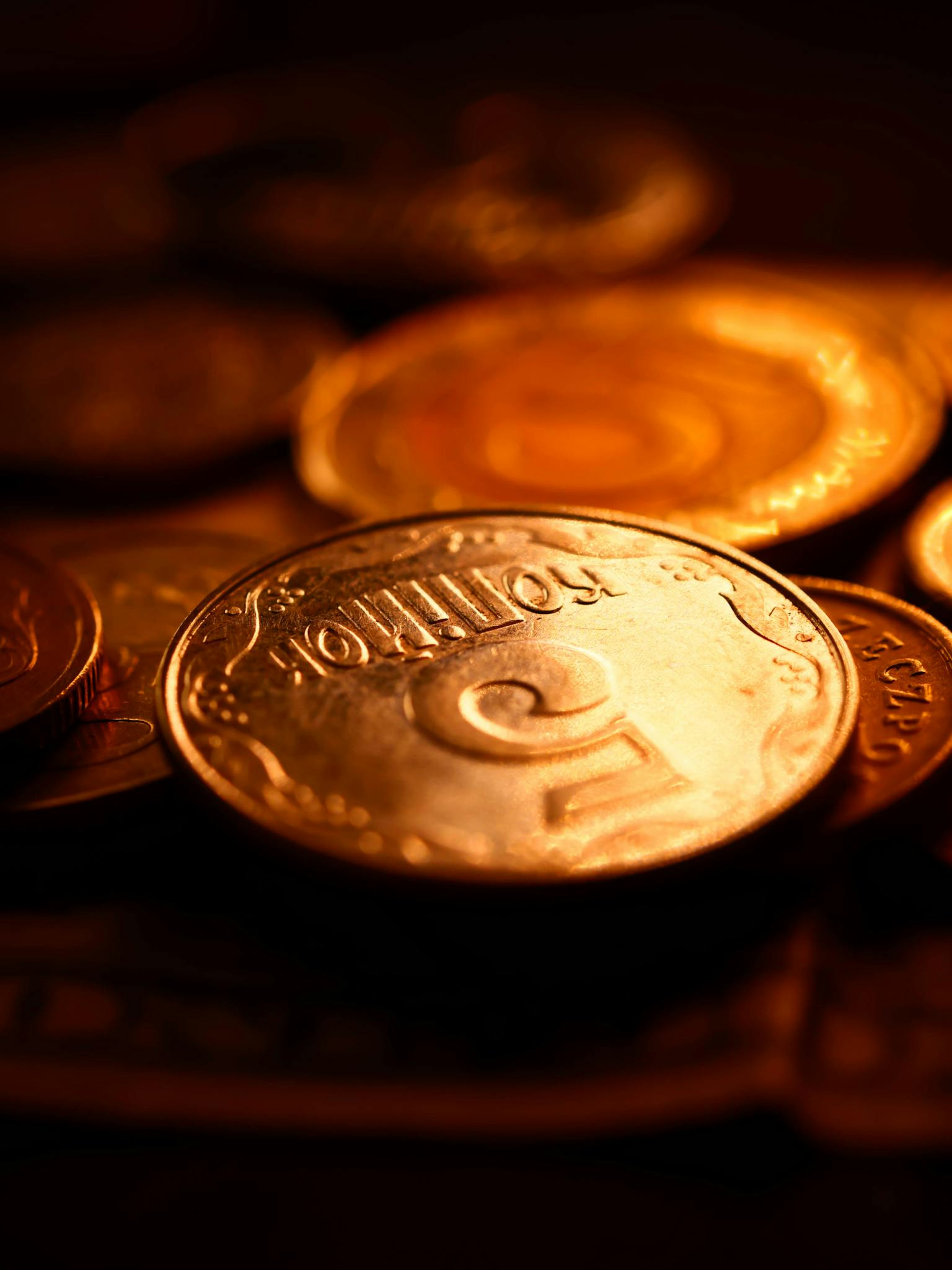 Macro view of various coins with warm lighting, highlighting currency details and textures.